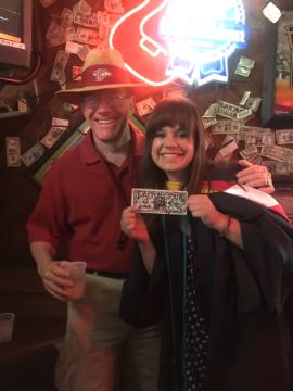 Two people smiling at a crowded event, one holding a sign reading Arthur De Lorimier 86.