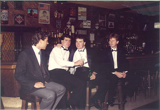 Four men in formal attire sitting at a bar.