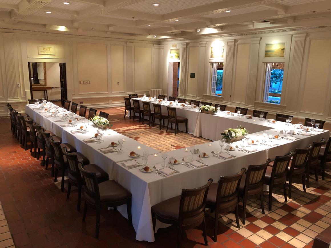 U-shaped table arrangement in a well-lit room with white tablecloths.