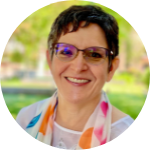 Person wearing glasses and a colorful scarf, smiling outdoors.