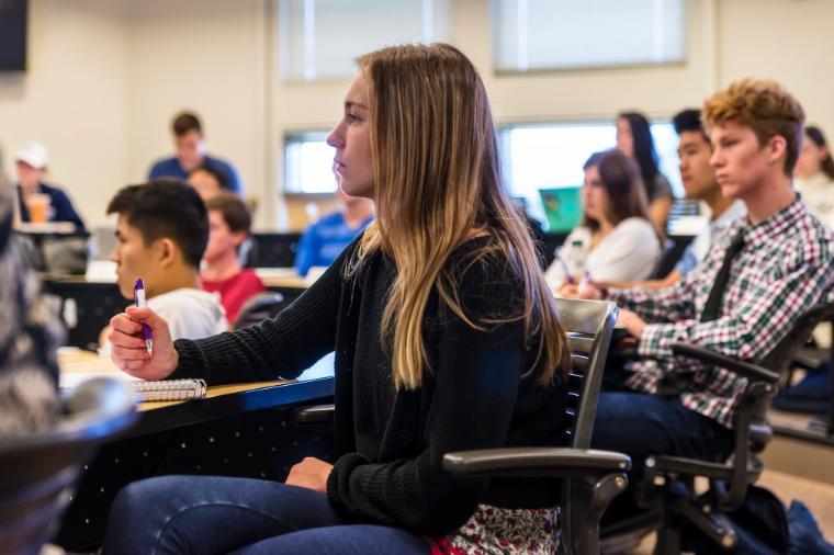 Student sitting in a class room paying attention to a lecture out of frame