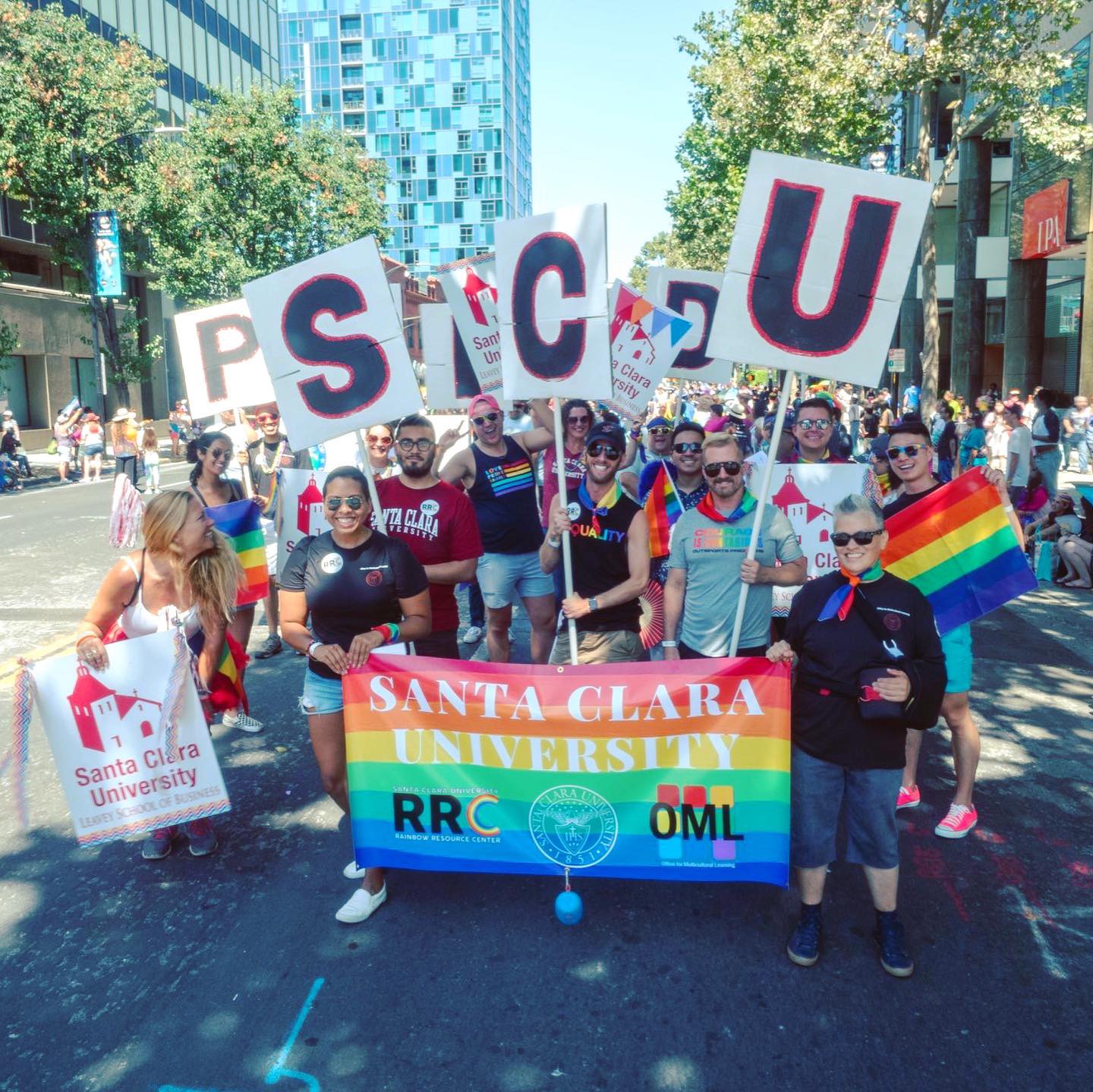 A group of people marching with P R I S C U signs and a rainbow banner.