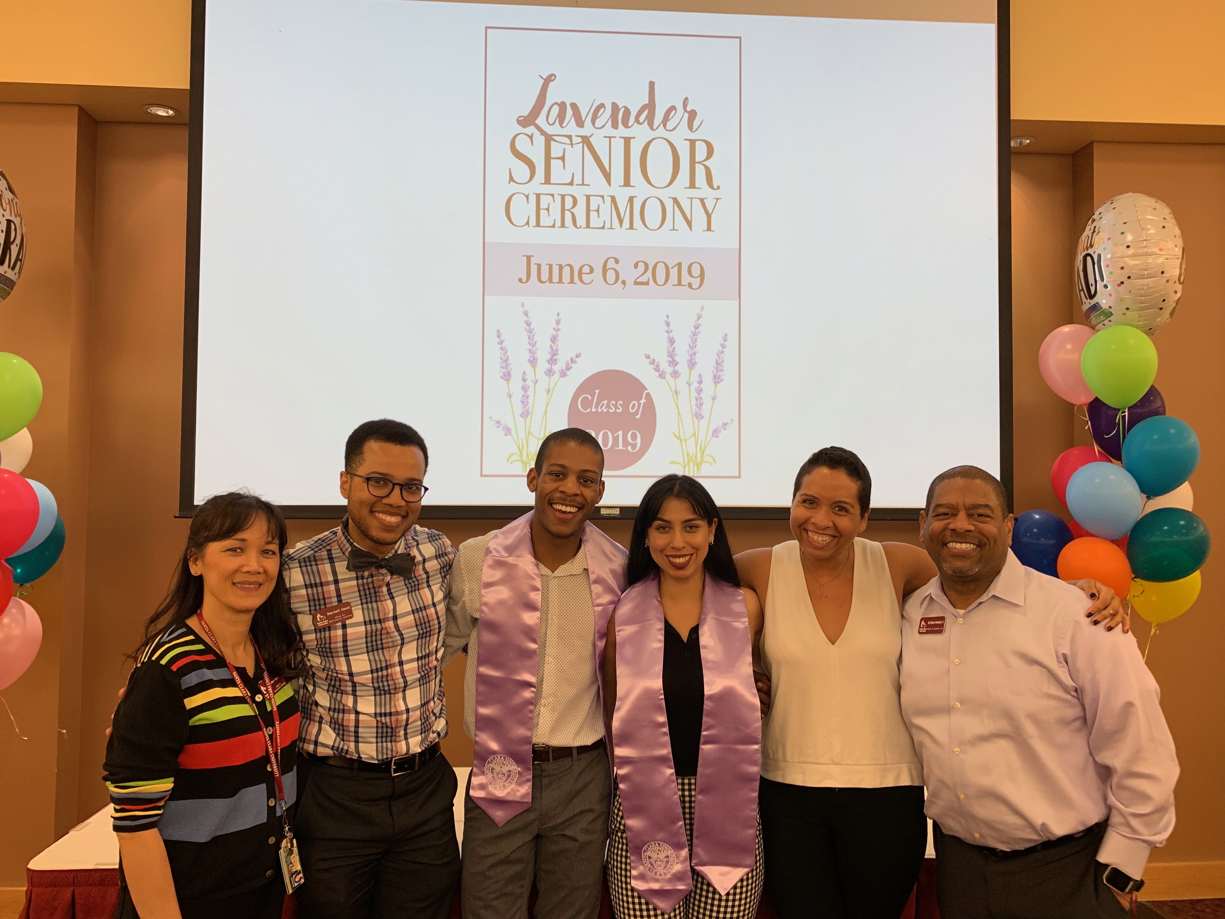 A group of people standing in front of a screen that says Lavender Ceremony.
