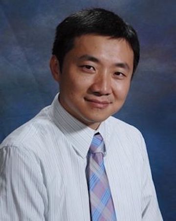 A professionally dressed person smiles against a studio background.