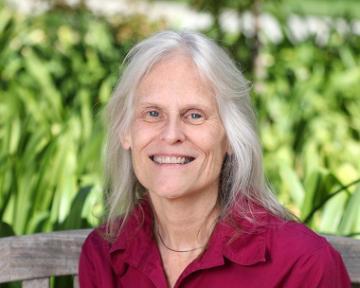 Woman smiling in front of a green leafy background.