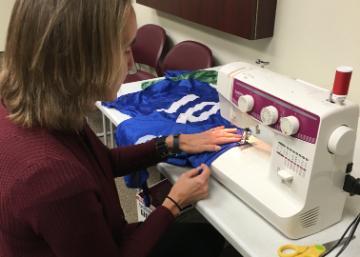 Person sewing on a machine with blue fabric labeled IM pennies.