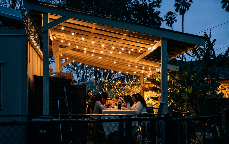Students eating a Nourish Night meal at night on the the Forge Garden deck, illuminated by string lights.