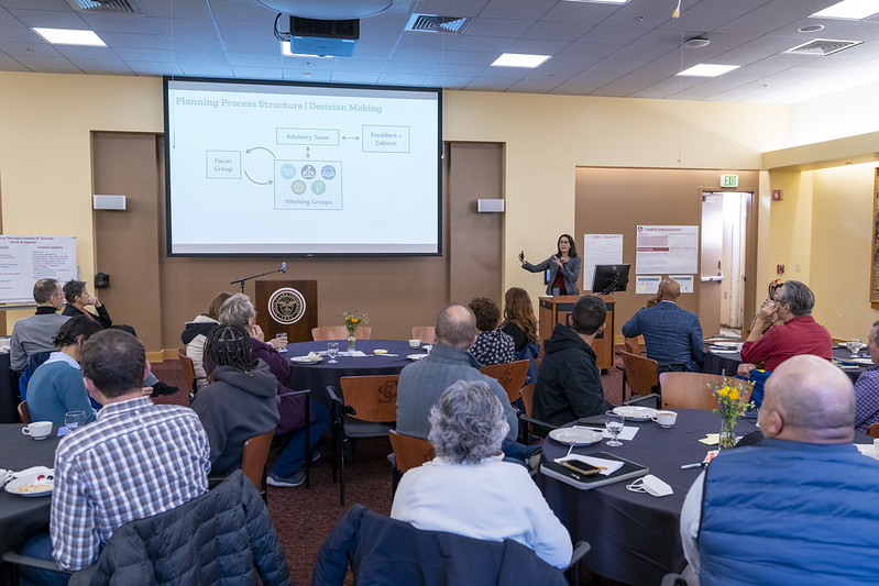 a person speaking into a hand-held microphone referencing a screen projection