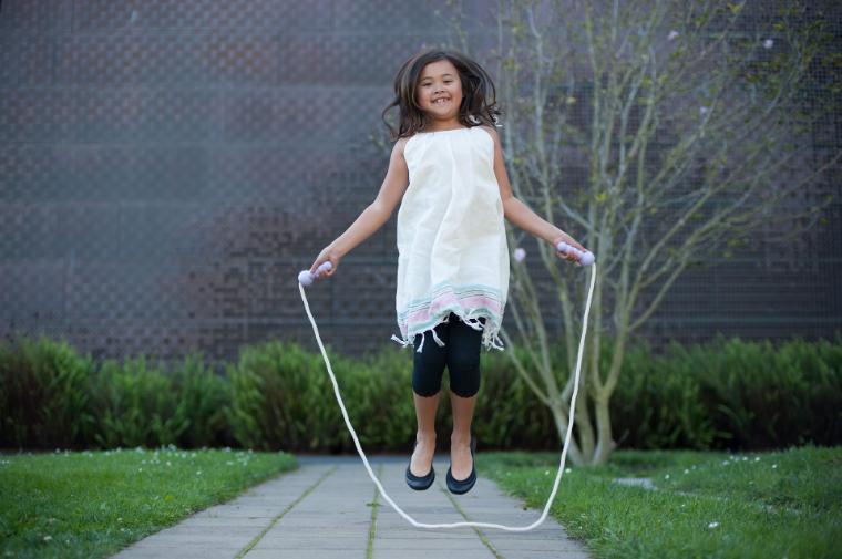 A girl jumping rope on a pathway outdoors.