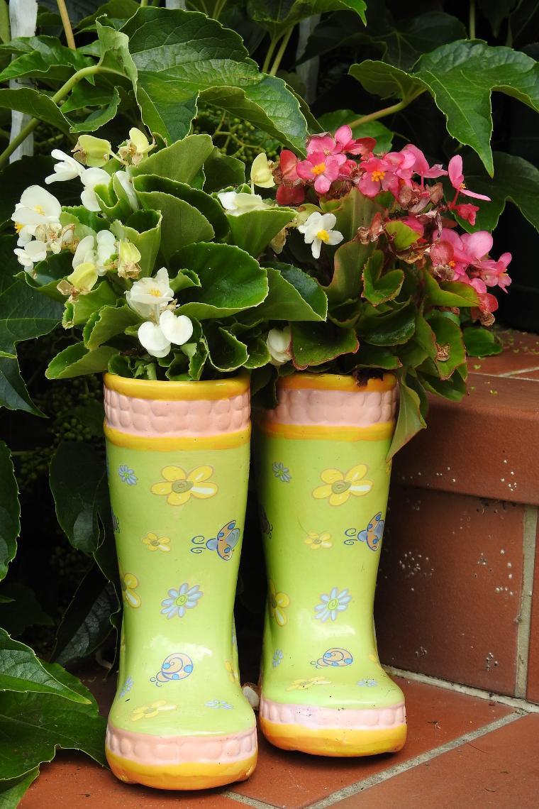 Two yellow rubber boots used as planters with flowers and plants.