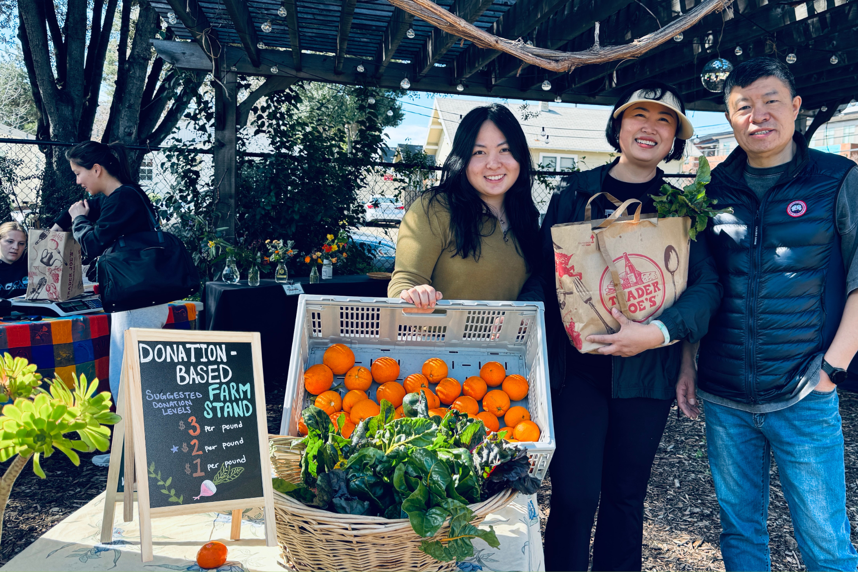 A student and her parents smiling behind of a table of produce at the farm stand