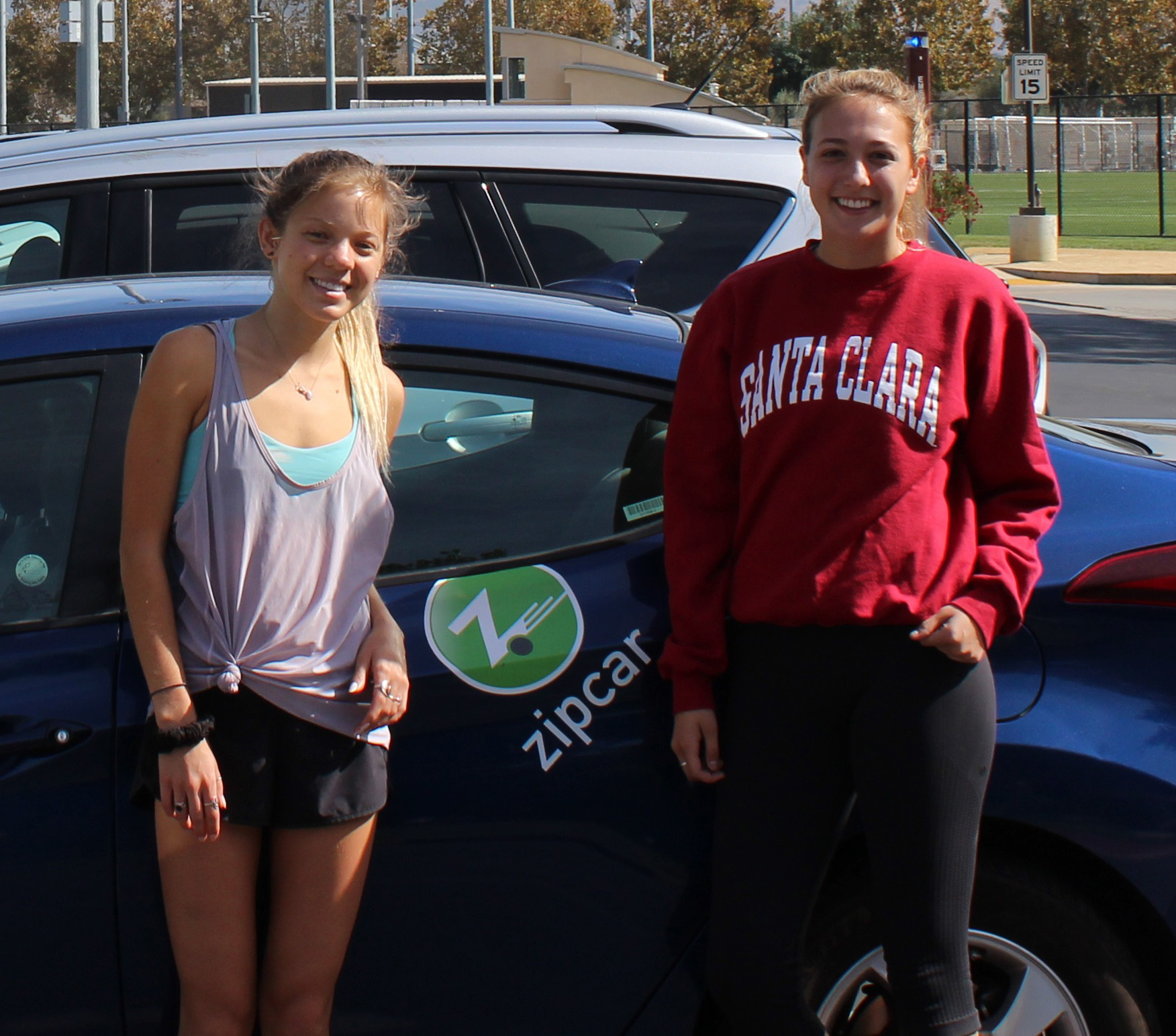 Two people standing next to a Zipcar vehicle.