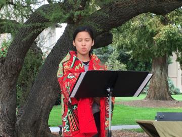 Alumna wrapped in red blanket reads Laudato Si under a tree