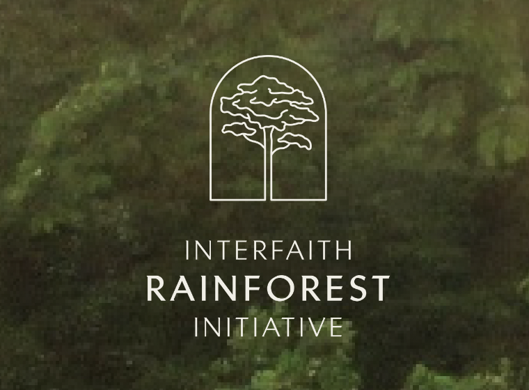 A white outline of a tree within a dome shape and the words, Interfaith Rainforest Initiative written below, with green leaves in the background