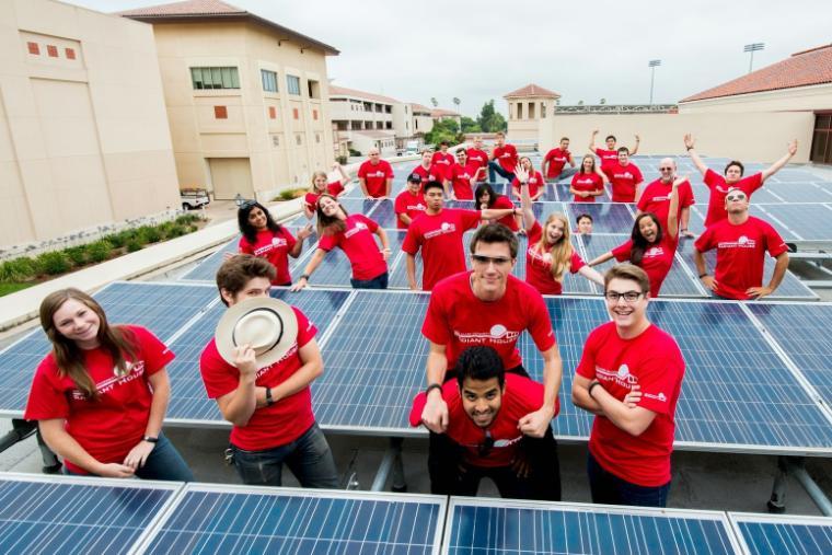 Group of people wearing red shirts, posing playfully on solar panels.