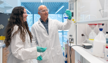 Professor Tillman and a student inspect a beaker of blue fluid