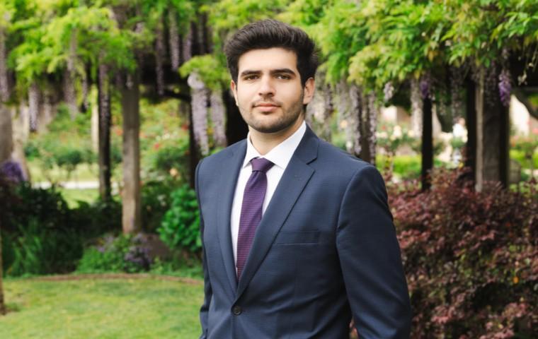 A man in a blue suit and purple tie standing in the mission gardens