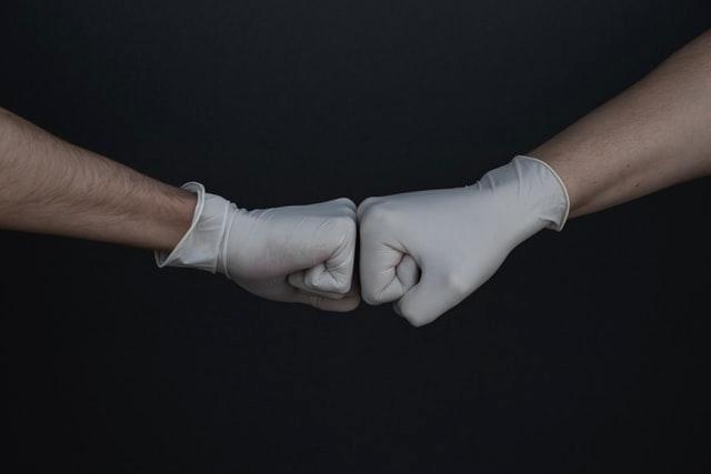 Photo of two fists in rubber covid-19 gloxes.