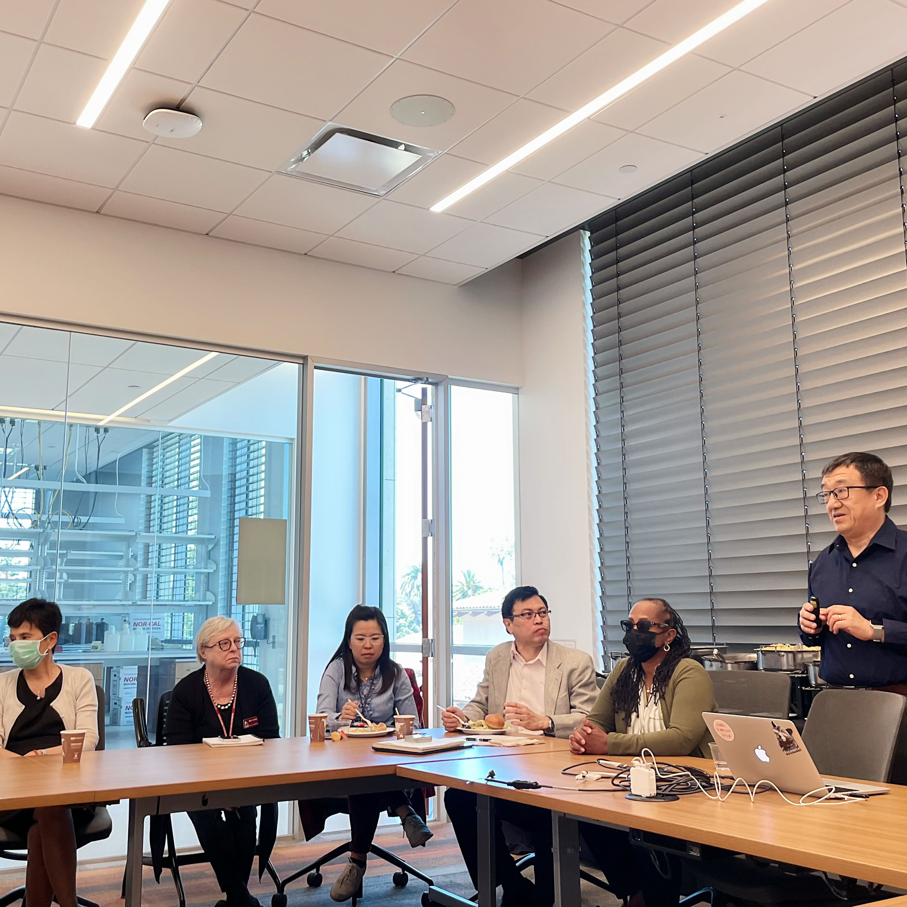 A person stands speaking to a group seated at a conference table.