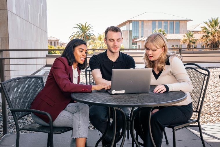 Students collaborating over a laptop on a terrace on campus