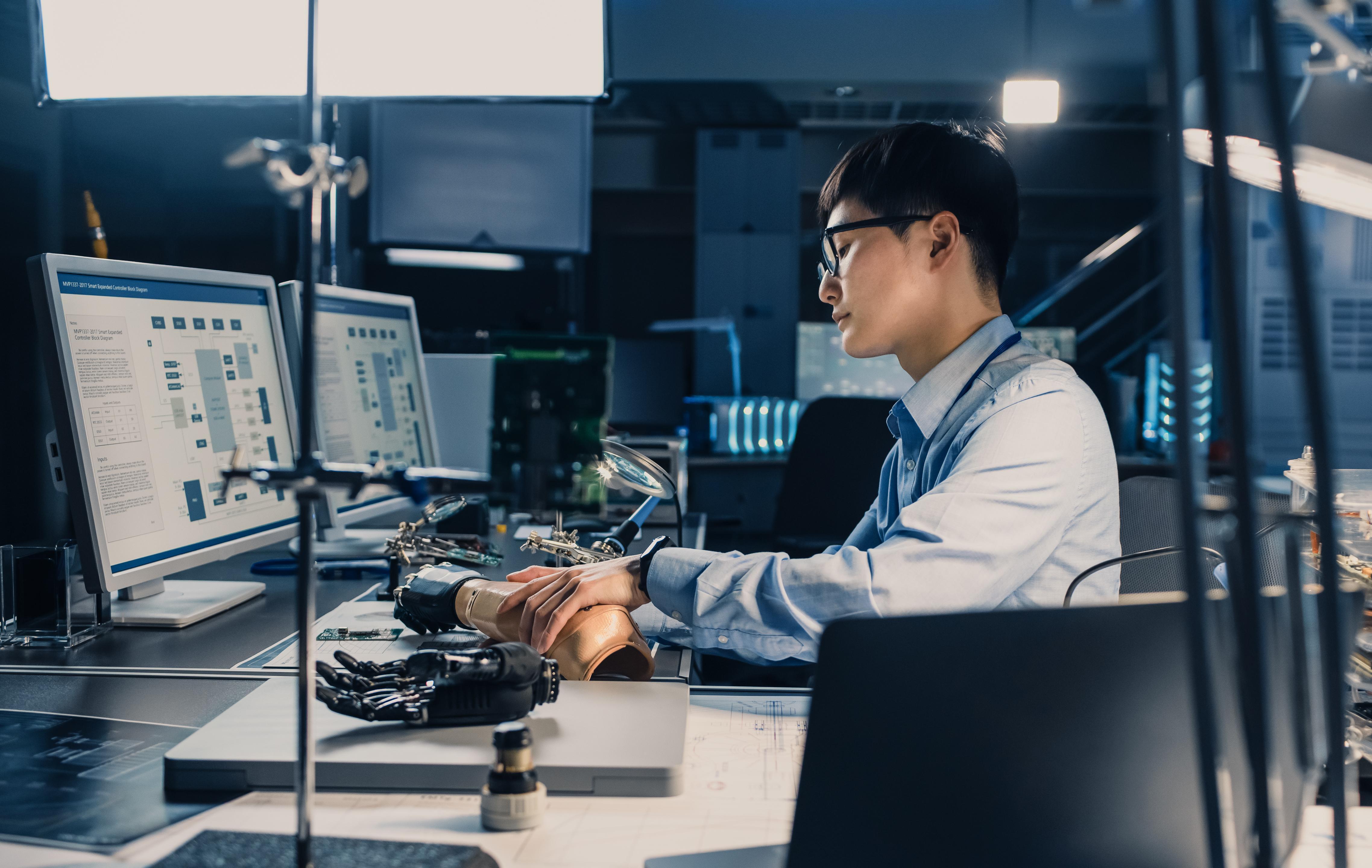 Student working on a computer with a robotic hand nearby