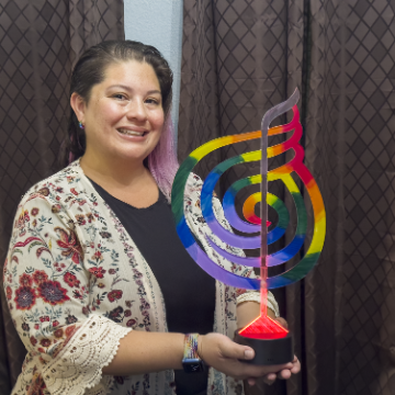 Person holding a colorful spiral sculpture in front of curtains. image link to story
