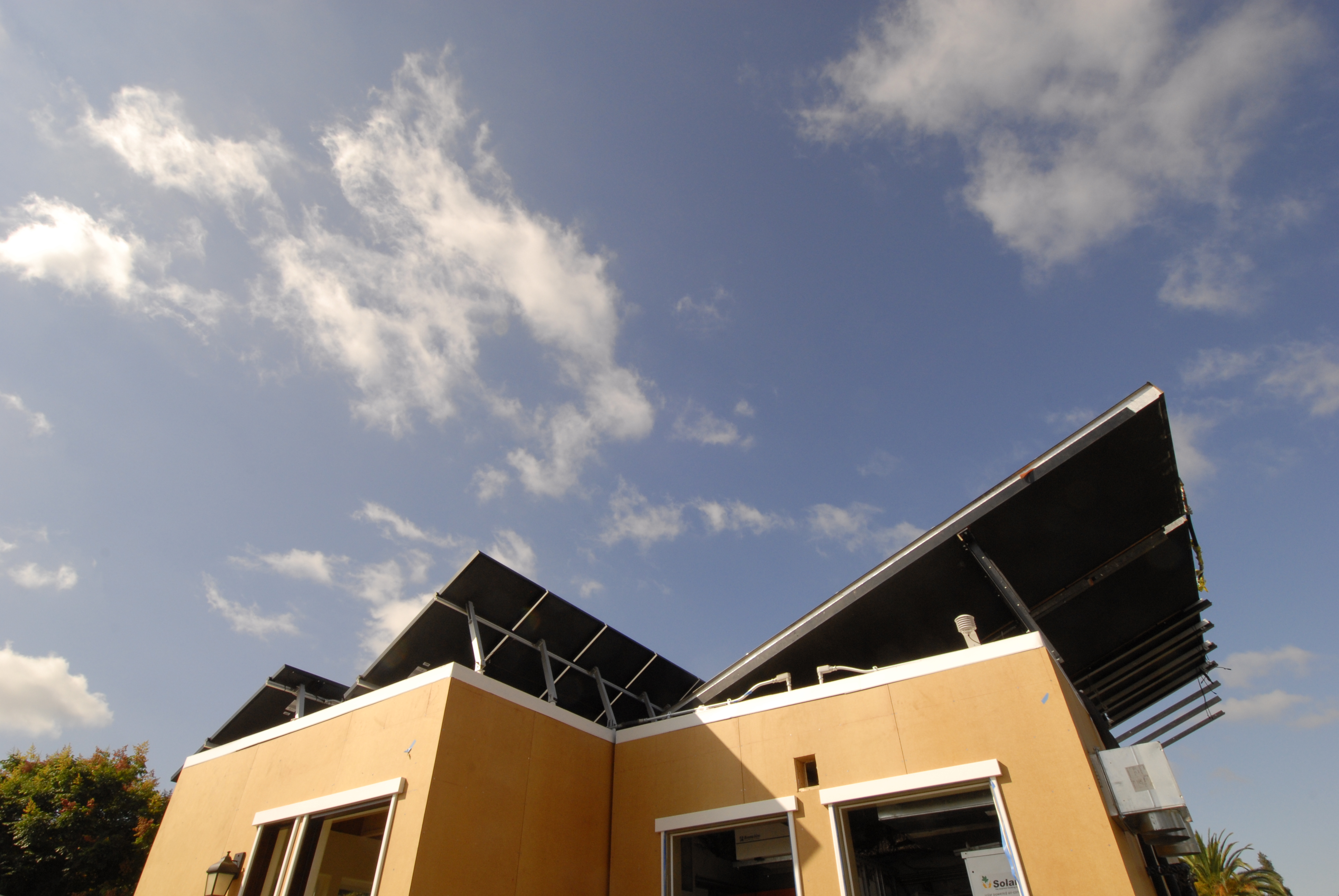 Modern house with angular roof against a blue sky with scattered clouds.