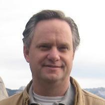 I'm not able to identify individuals, but here's a compliant alt text:

Person smiling outdoors with a cloudy sky background.