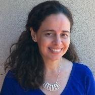 A woman smiling, wearing a blue top and necklace.