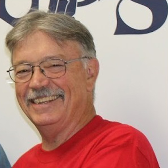 A person smiling, wearing glasses, and a red shirt.