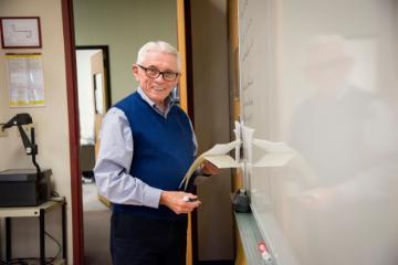 Man in an office walking through a doorway holding a notebook. image link to story