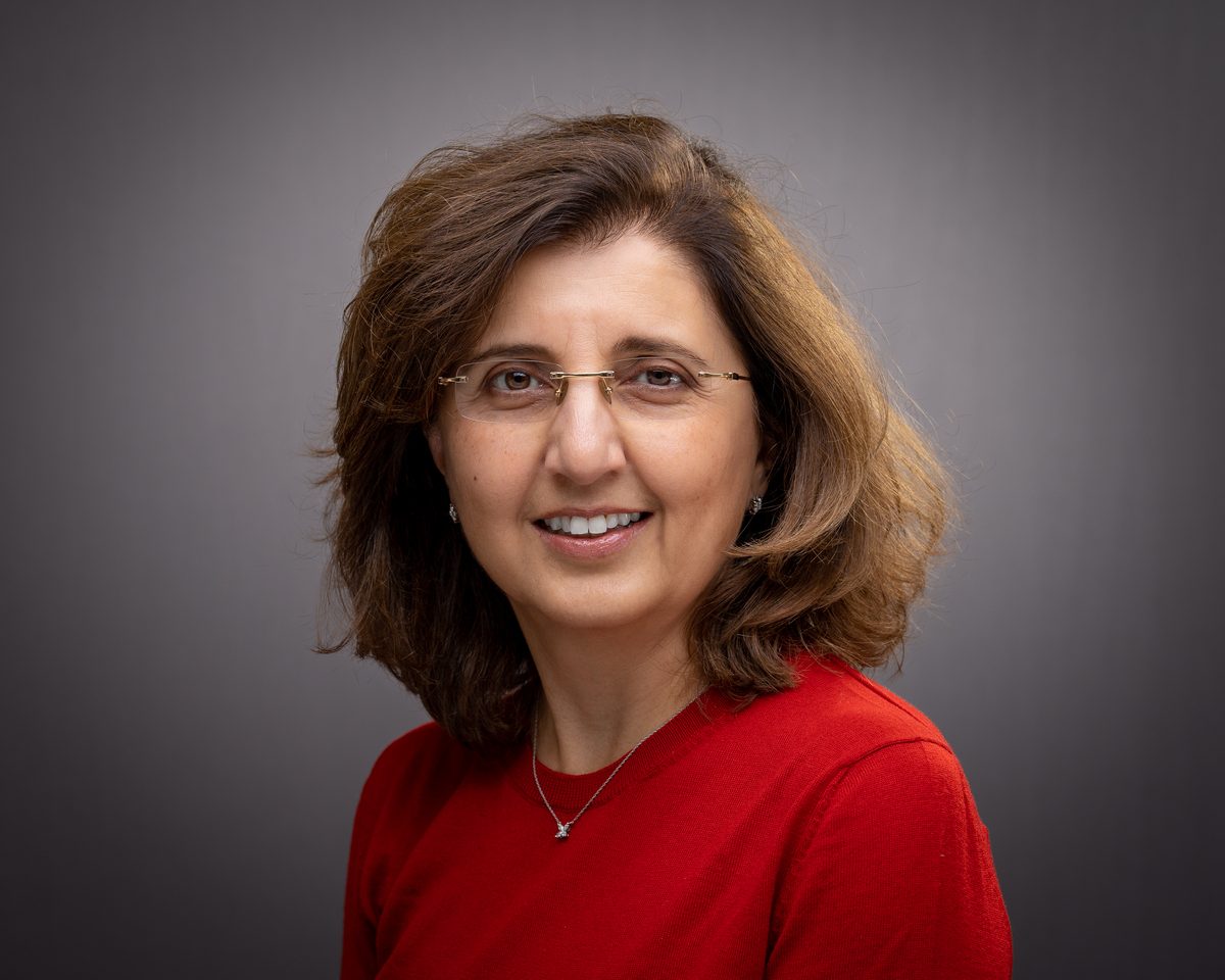 A woman in a red shirt smiles against a grey background.