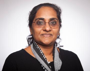 A person wearing glasses and a black top with a scarf.