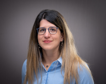 A person with glasses and long hair wearing a blue shirt.