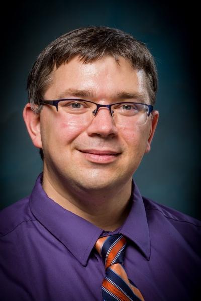 A person wearing glasses and a purple shirt with a tie.