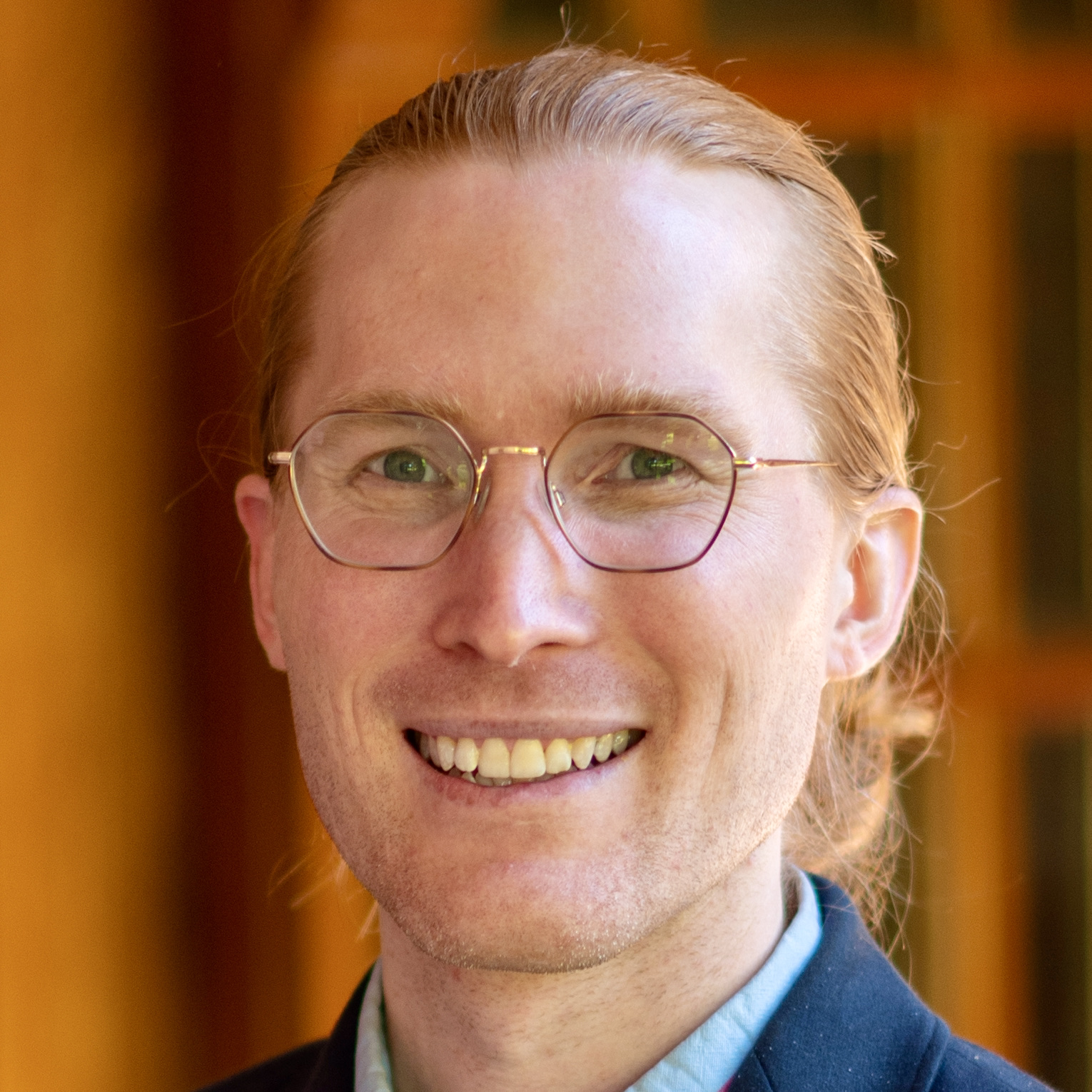 A smiling person with glasses looking to the right.