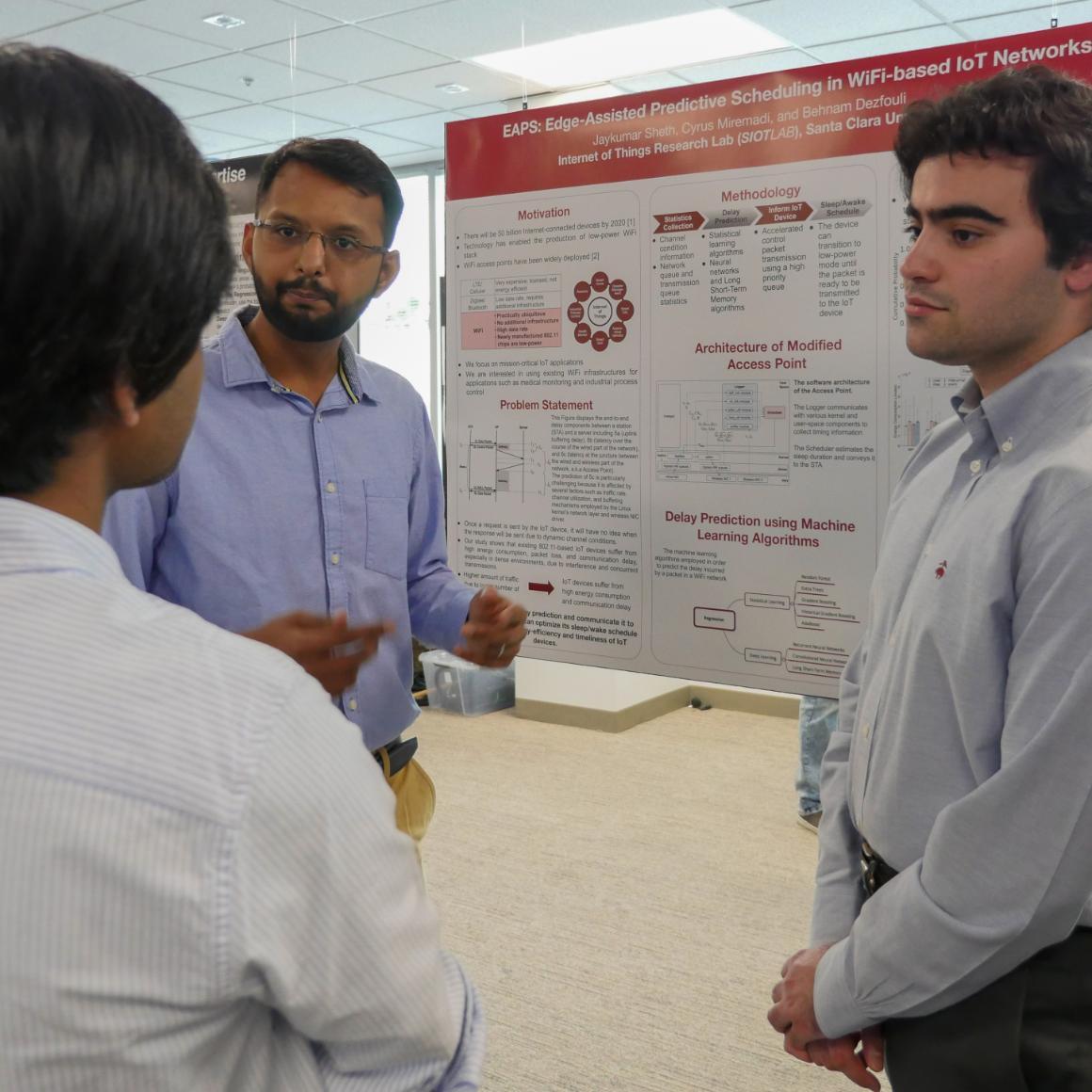 2 SCU student researchers stand in front of their poster, explaining their work to a visitor