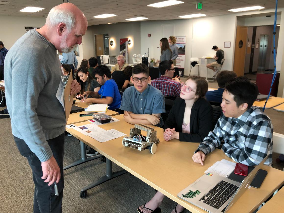 A group of people gathering around a table watching a robot demonstration.