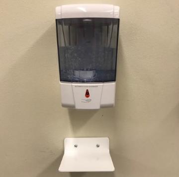 Wall-mounted dispenser with a catch tray installed below it.