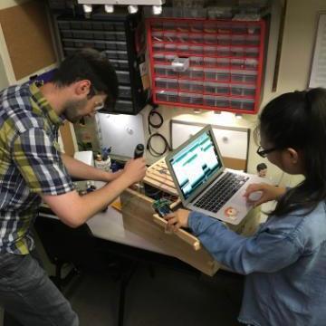 Two people work together at a table with electronic equipment.