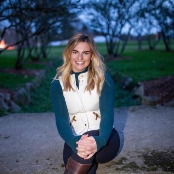 A person kneeling outdoors, smiling, with trees in the background.