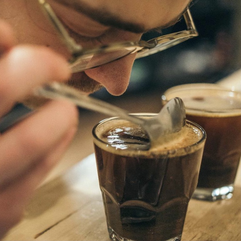 Person smelling coffee in a glass with a spoon.