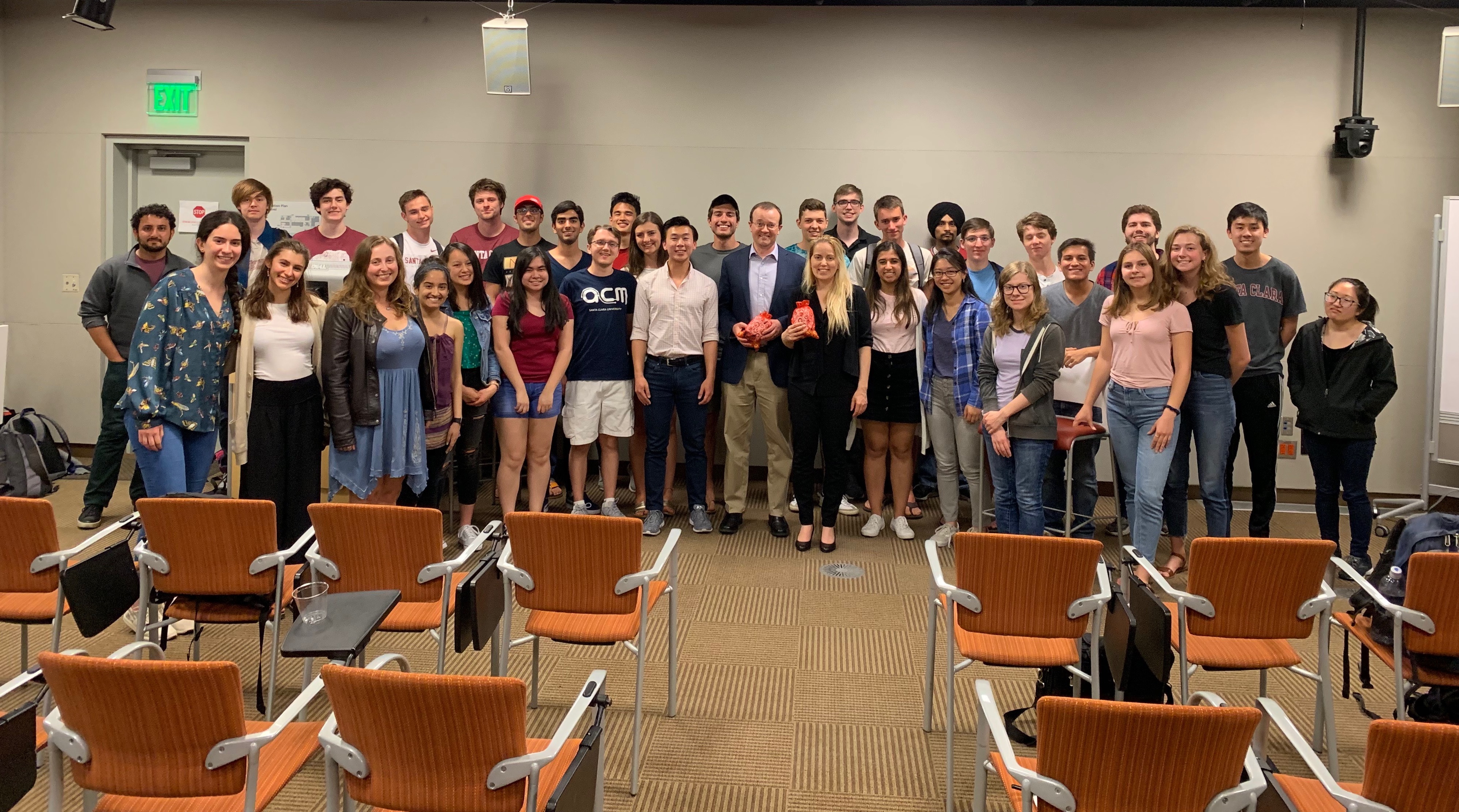 Group photo of people standing in front of an audience in a lecture hall.