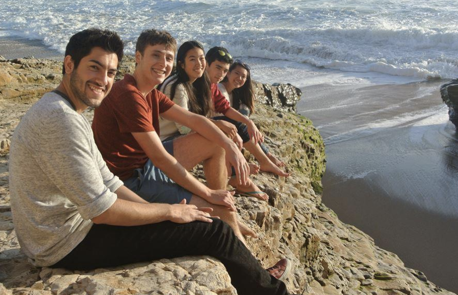 A group of people sitting on a cliff overlooking the beach.